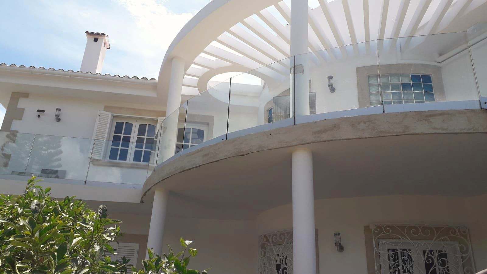 Balcón curvo de una villa blanca con barandilla de vidrio continua bajo una pérgola circular