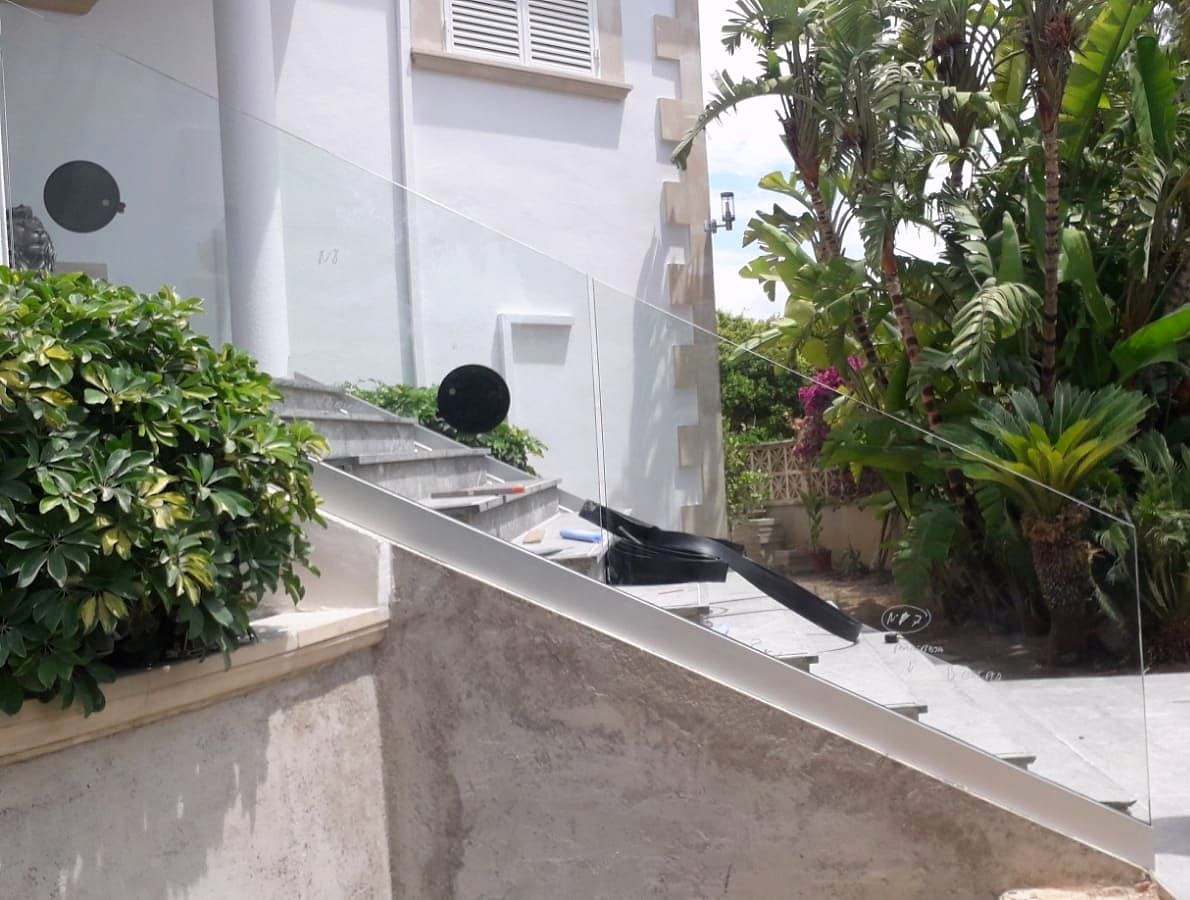 Barandilla de vidrio que baja en pendiente junto a una escalera exterior con plantas
