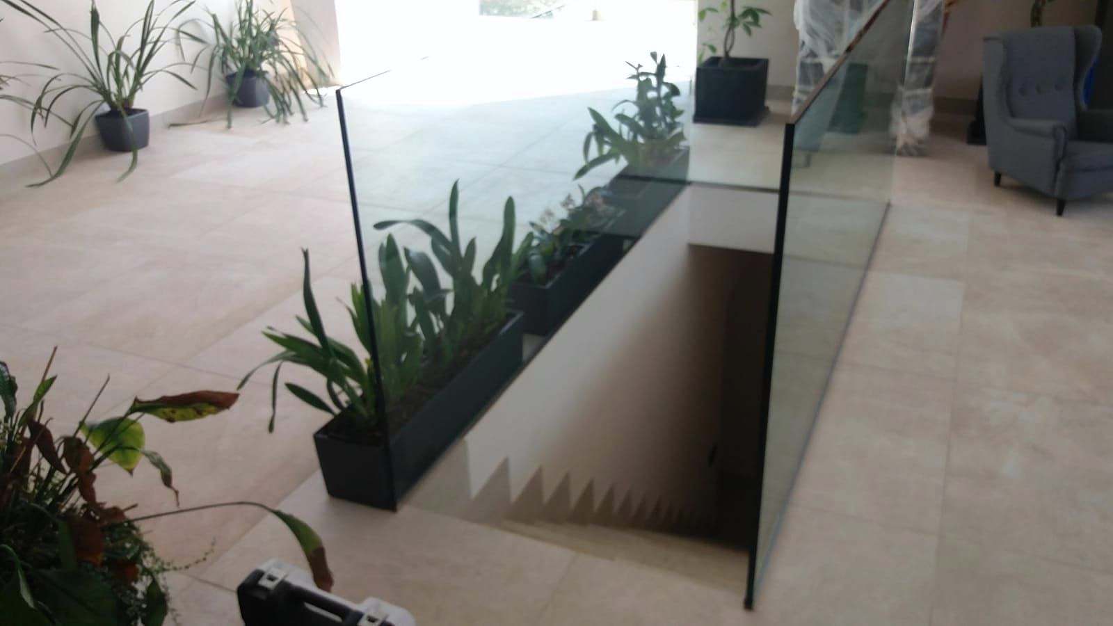 Hueco de escalera protegido por vidrio, rodeado de plantas en un salón luminoso