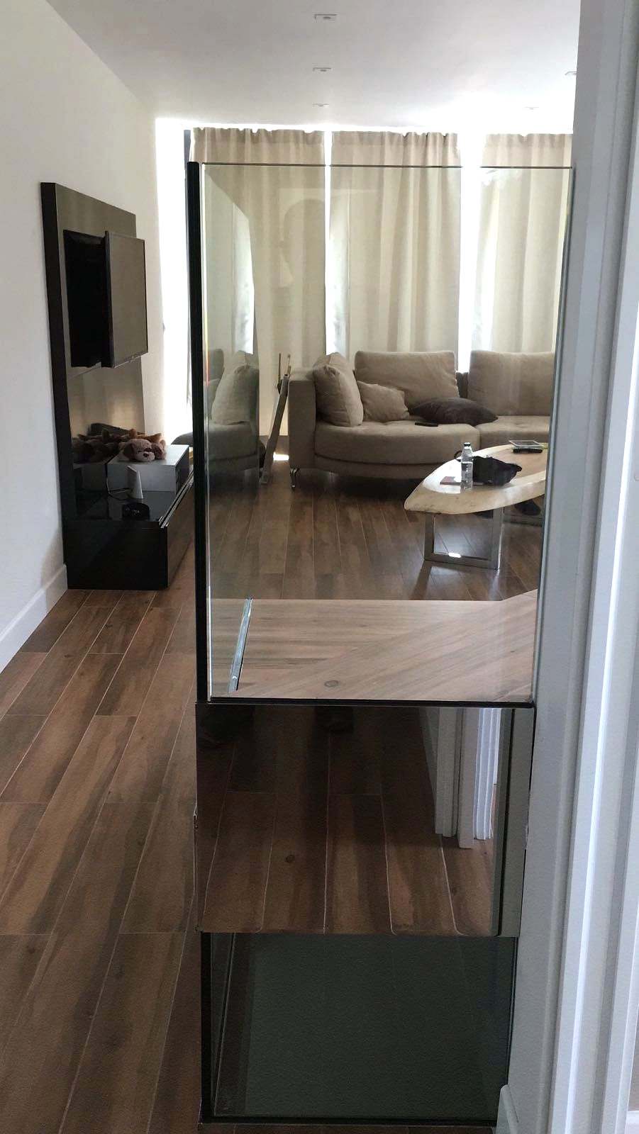 Salón con suelo de madera y barandilla de vidrio junto al hueco de la escalera