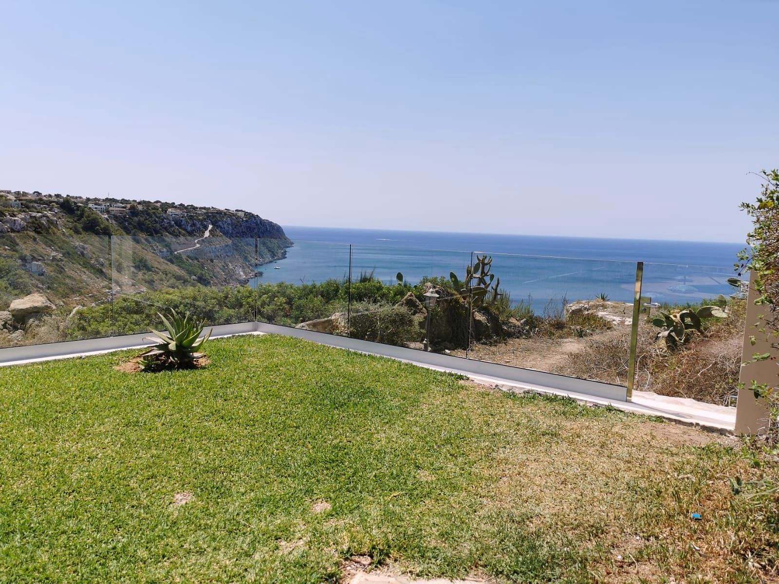 Jardín sobre un acantilado con barandilla de vidrio casi invisible frente al mar