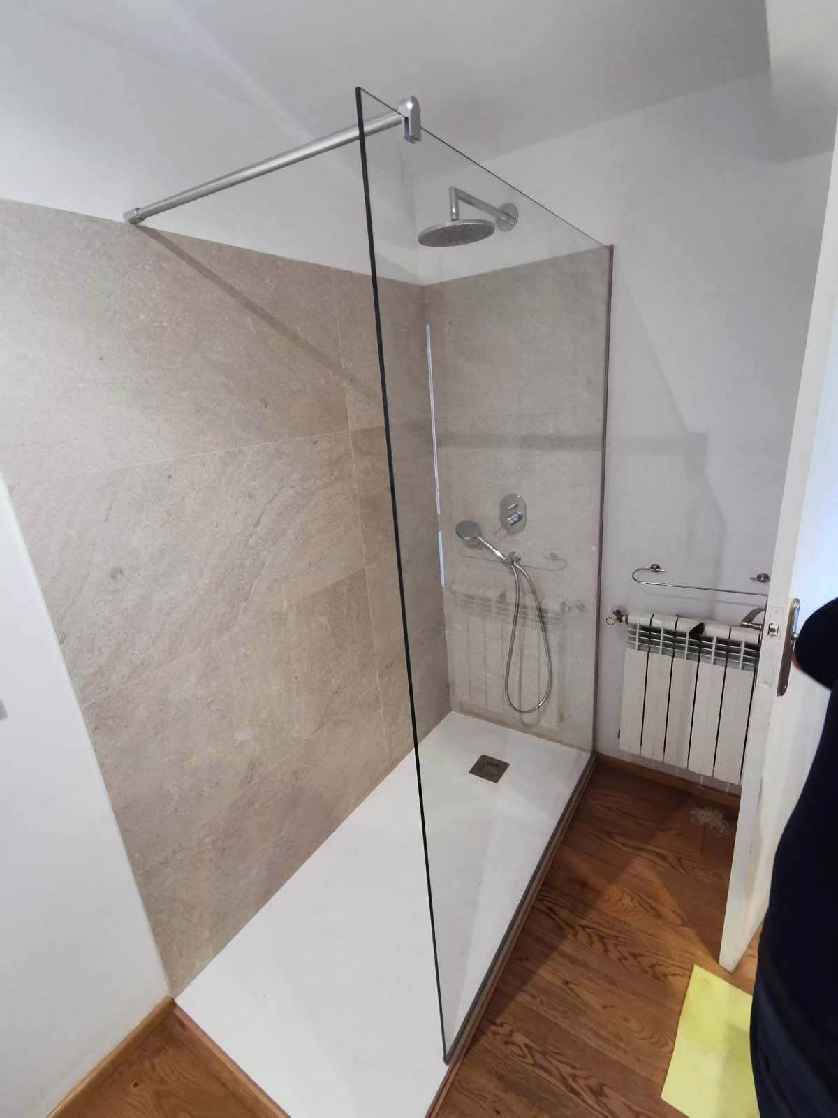Ducha de obra con un único panel fijo de vidrio sujeto por una barra al techo