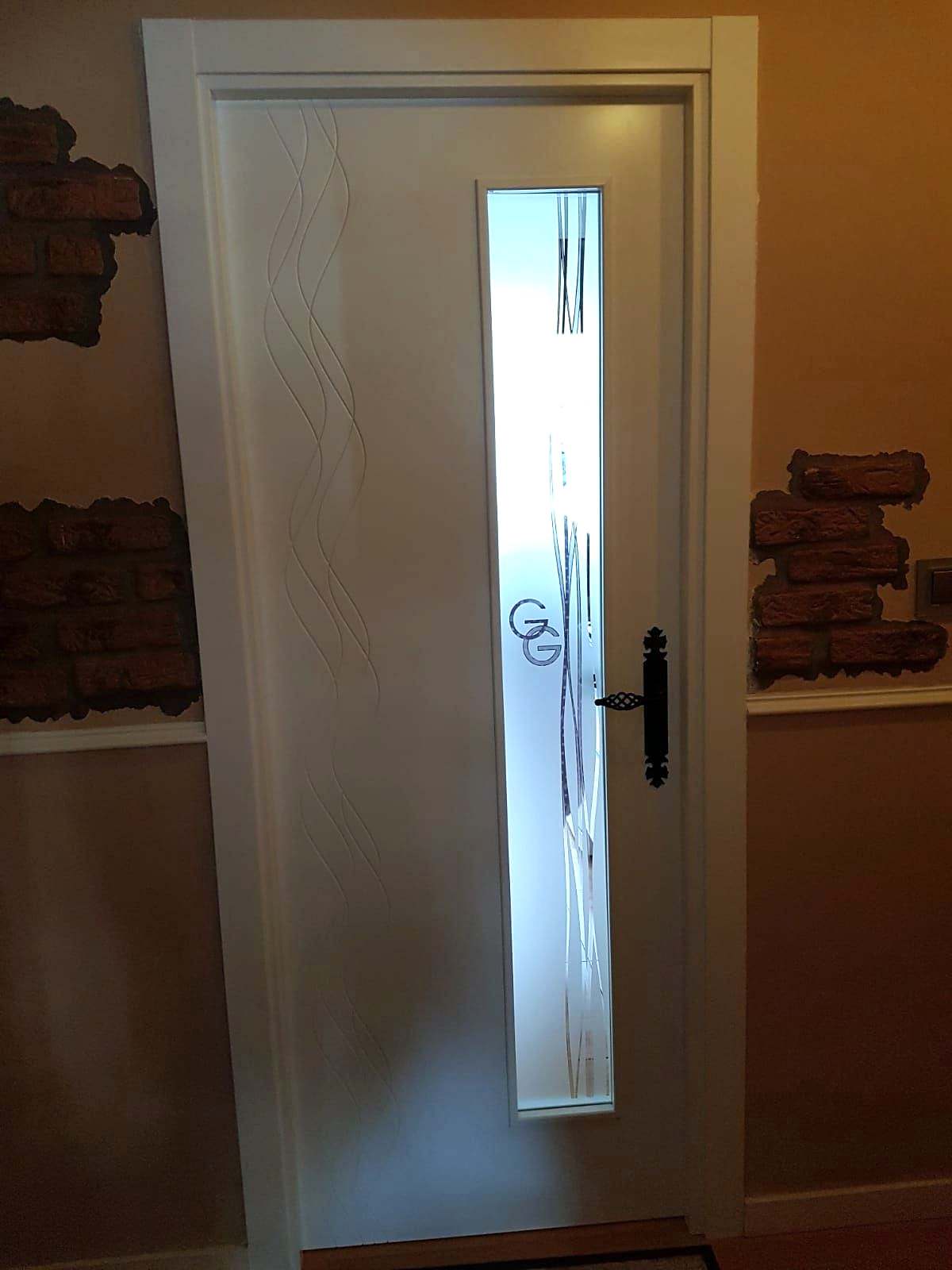 Puerta blanca con un vidrio vertical estrecho decorado con iniciales grabadas